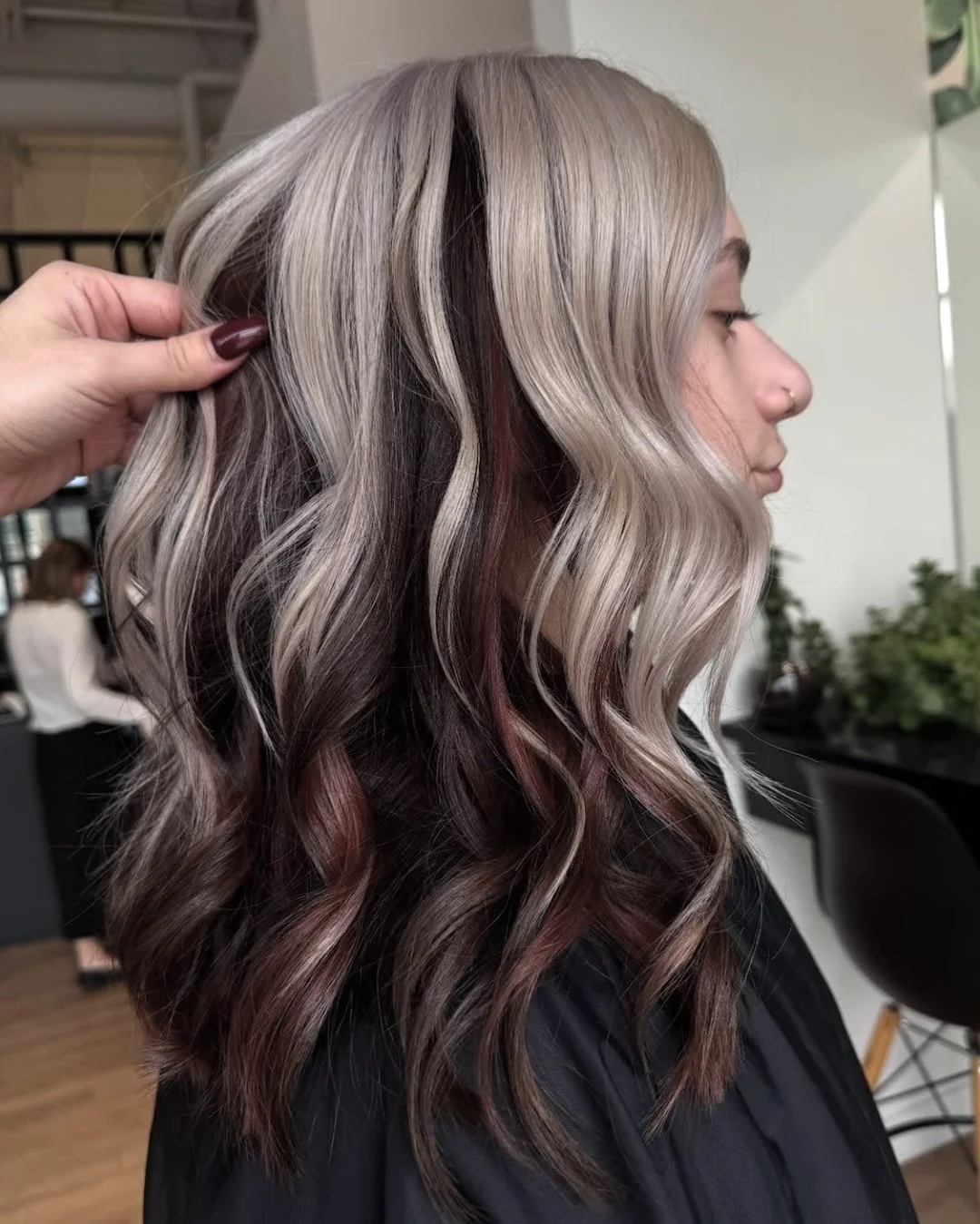 Side view of a woman with shoulder-length wavy hair styled with various shades of blonde, brown, and pink, in a salon.