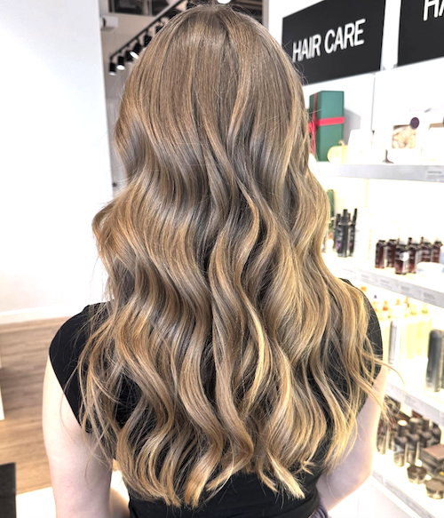 Back view of a woman with long, wavy, light brown hair in a hair care store