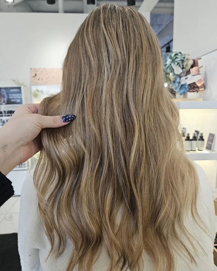 Back view of a woman with long, wavy, blonde hair inside a salon.