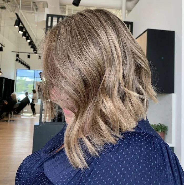 A woman with shoulder-length, wavy blond hair wearing glasses inside a hair salon.