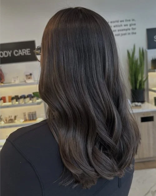 Woman with long, wavy dark brown hair standing in a beauty store or salon
