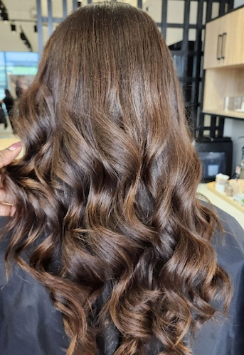 Back of a woman with long, wavy, brown hair in a salon setting.