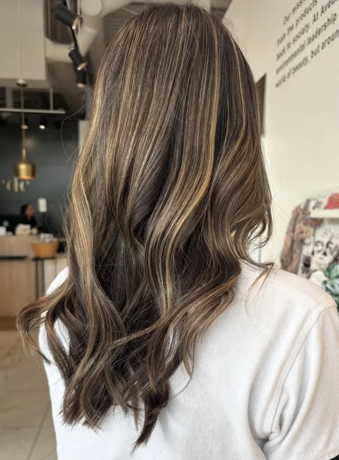 Side view of wavy, balayage hair with caramel and light brown highlights on a woman in a salon.