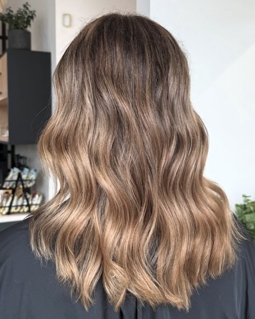Back of a woman's head with shoulder-length, wavy, light brown hair with subtle highlights.
