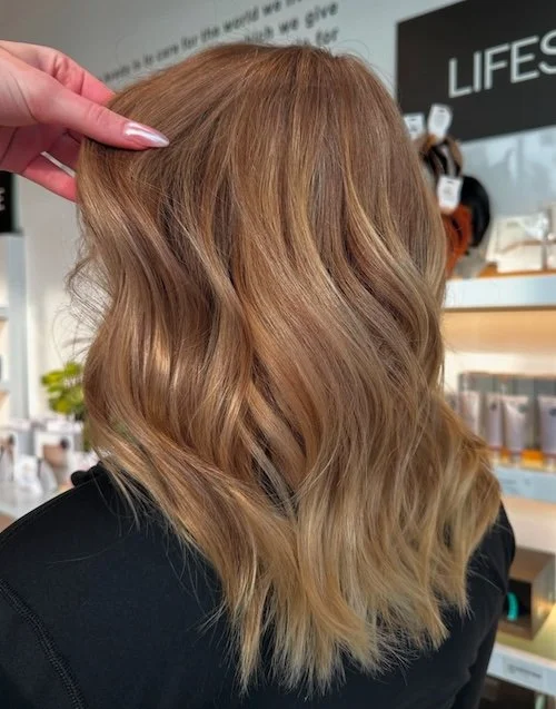 Close-up of a woman with shoulder-length, wavy, light brown hair in a salon.