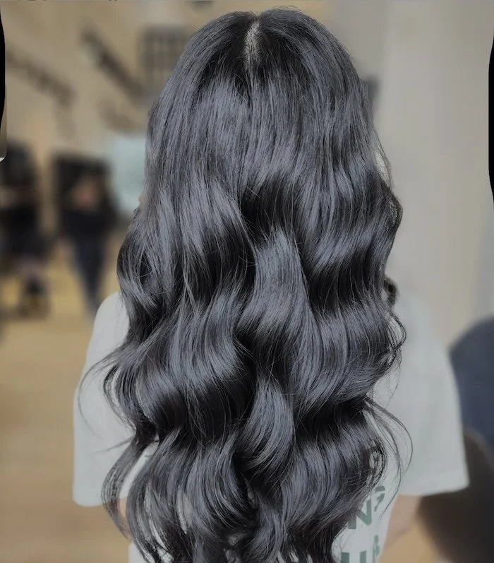 Back of a person's head with long, shiny, black wavy hair.