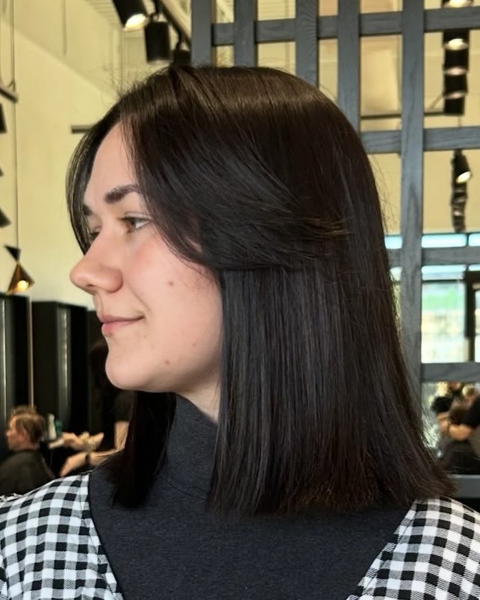 a woman with straight, dark brown hair, wearing a black turtleneck and a checkered shirt, in a salon.