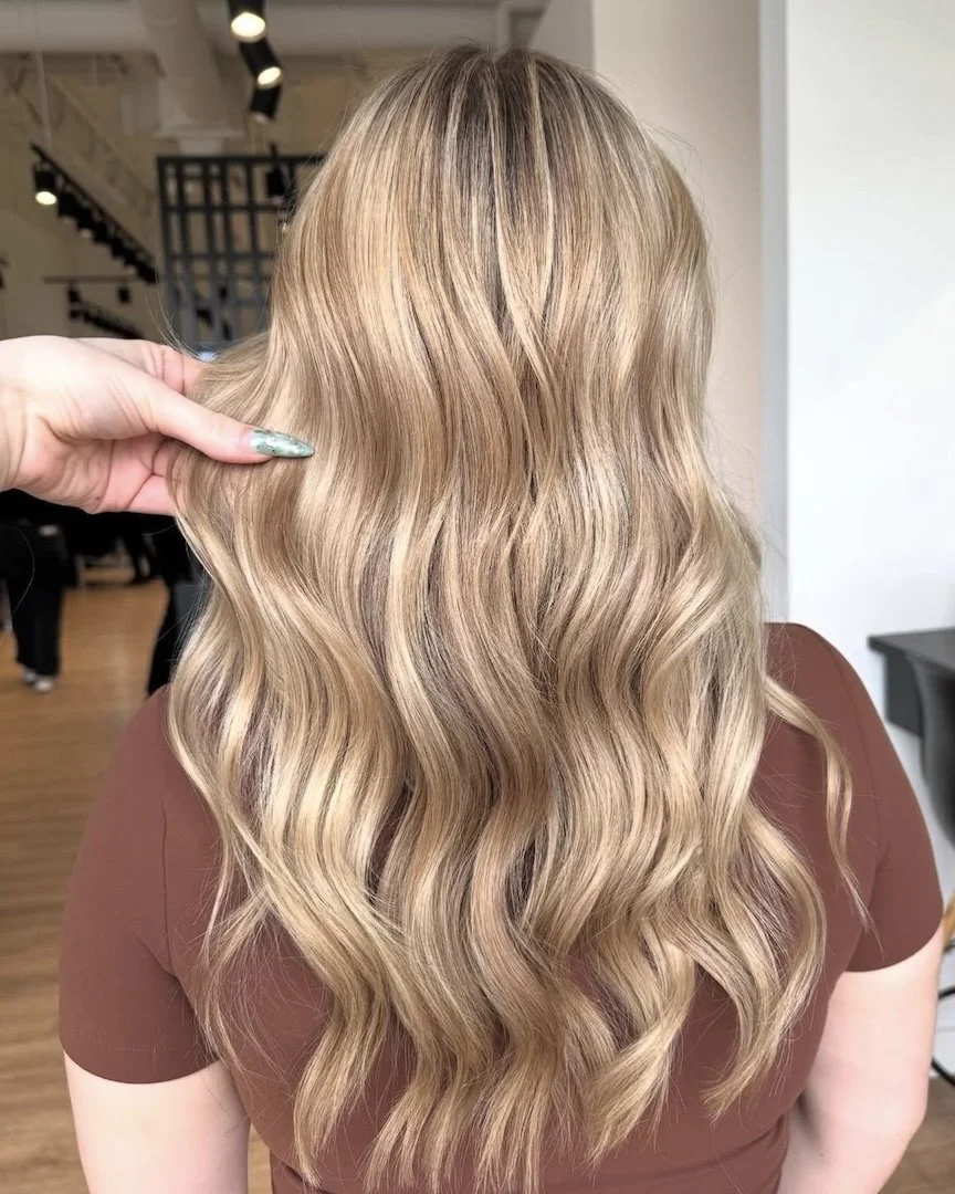 Back of a woman's head with long, wavy blonde hair, being styled at a salon.