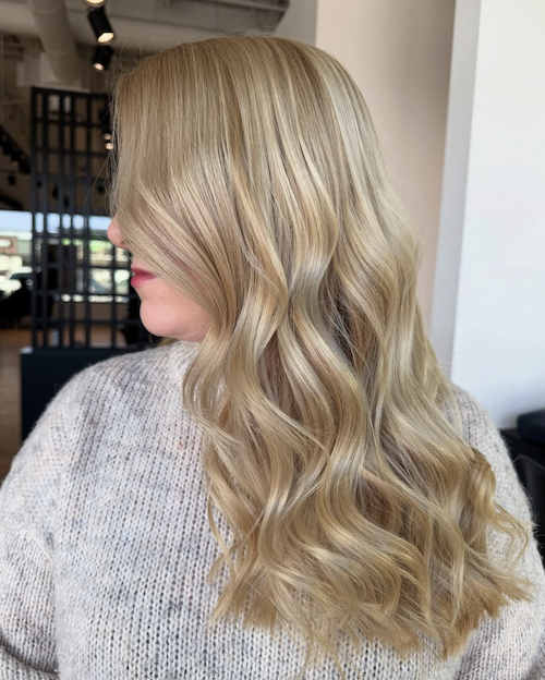 Side view of a woman with long, wavy blonde hair wearing a gray sweater.