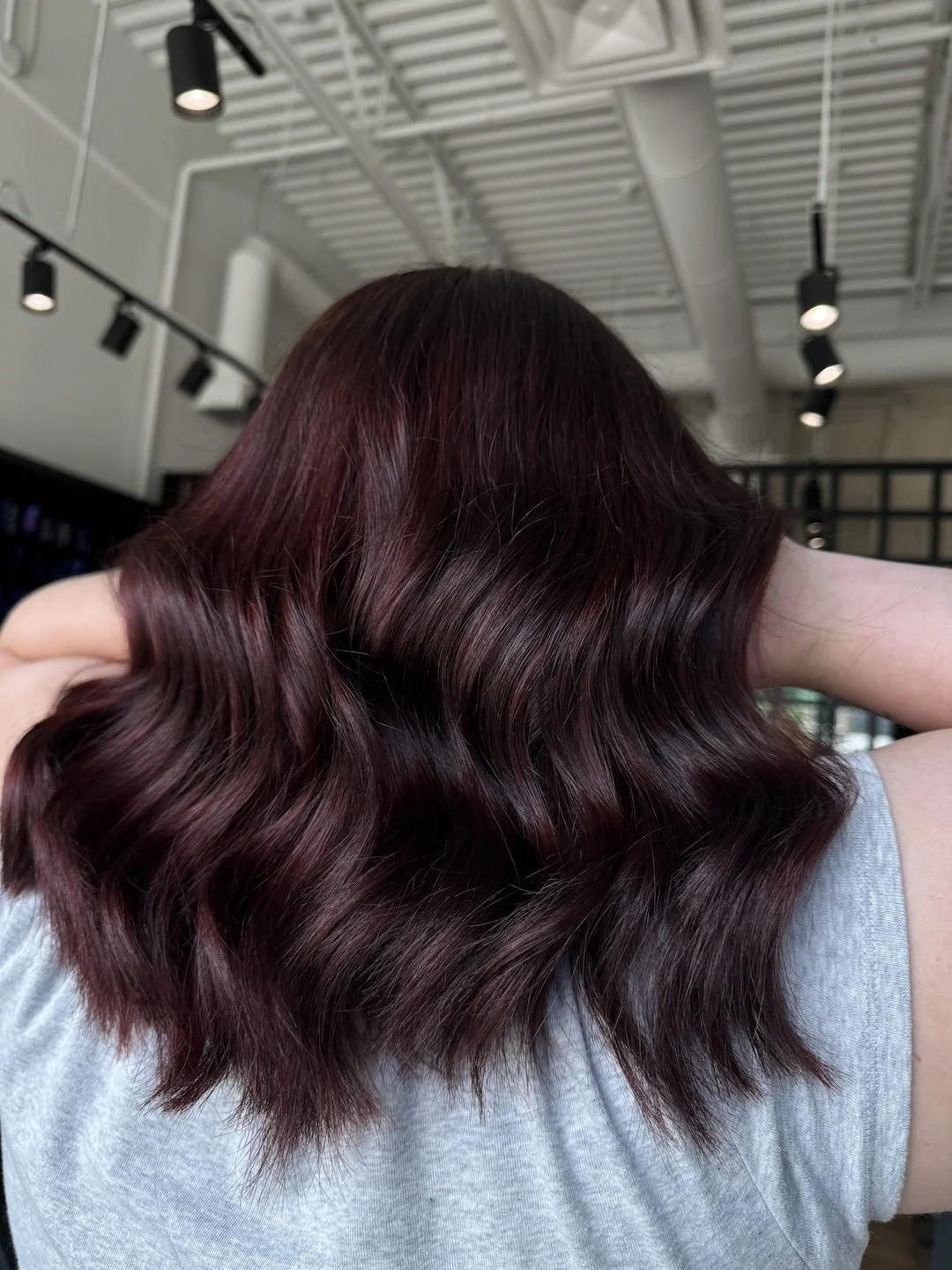 Back view of a person with shoulder-length, wavy burgundy hair in a salon.
