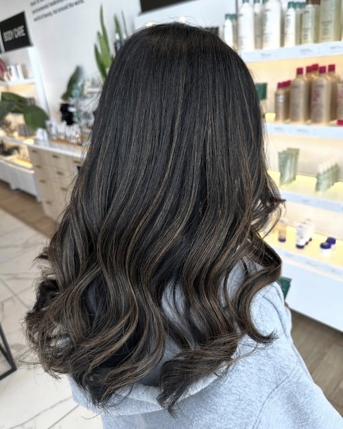 Back of a woman with long, dark, wavy hair in a store or salon setting.