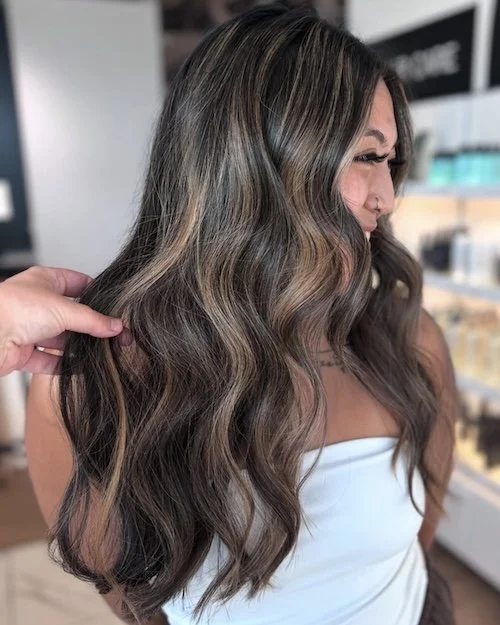 Woman with long, wavy hair in shades of brown and blonde, at a hair salon.