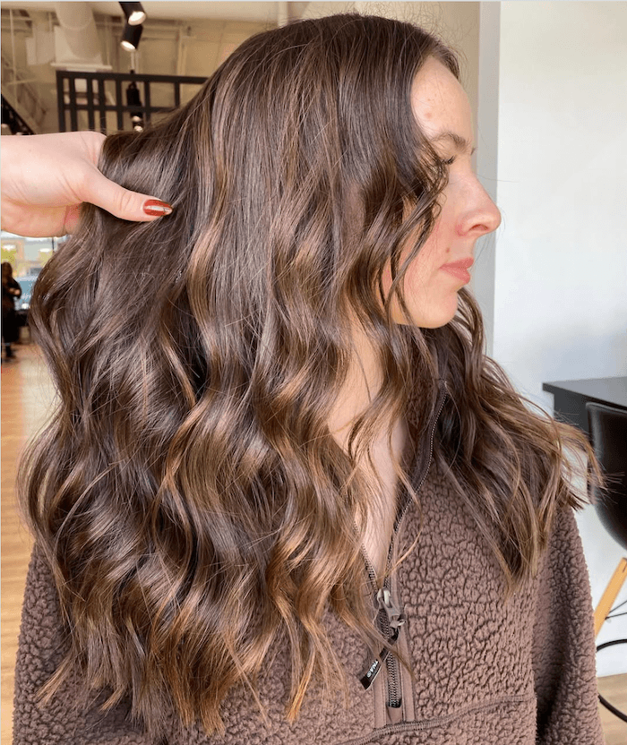 Woman with long, wavy brown hair being styled at a salon.