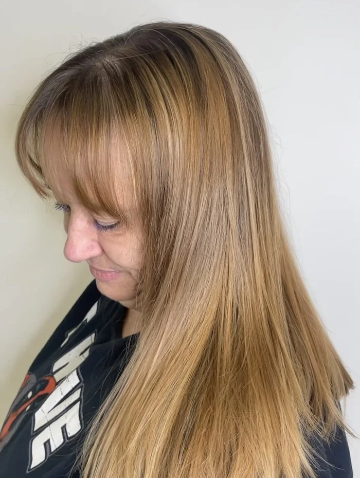 Profile of a woman with long, straight, blond hair and bangs, looking down.