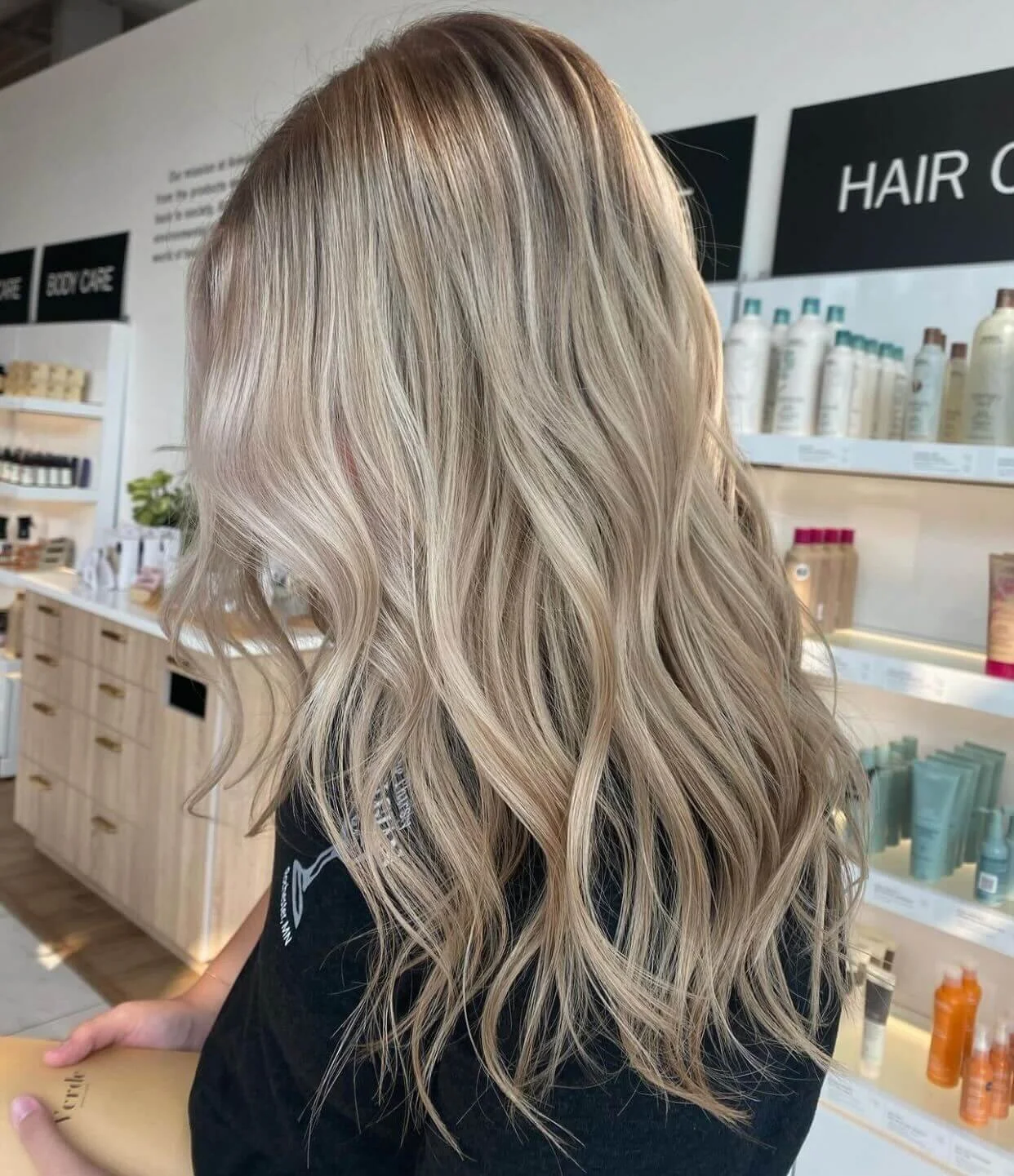Back view of a woman with long, wavy blonde hair inside a haircare store.
