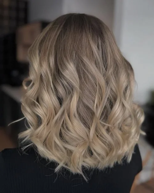 Back view of a woman's blonde wavy shoulder-length hair.