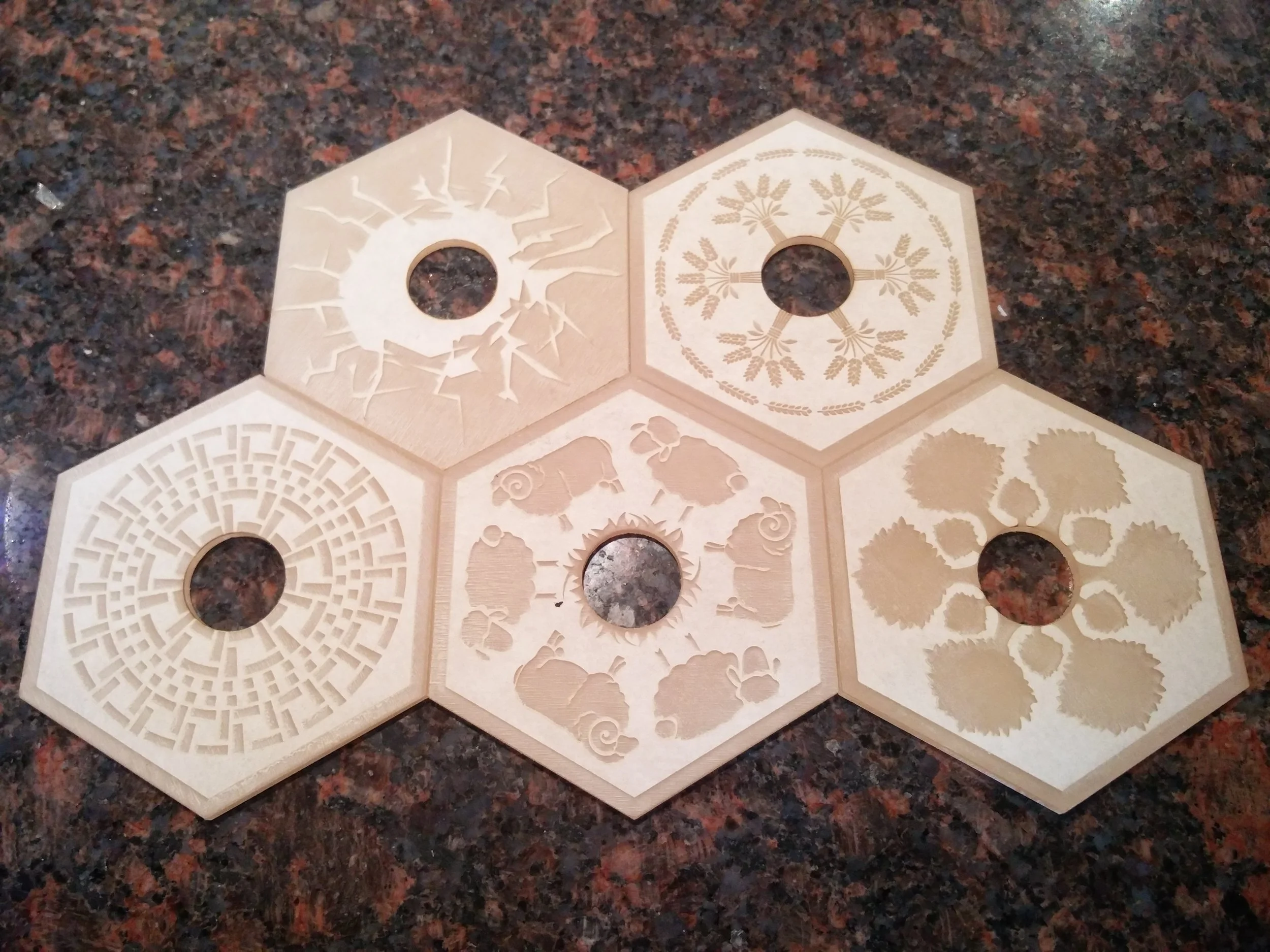  The designs on these hexagonal pieces represent the 5 different resources acquired in the game.   Top Left:  Ore    Top Right:  Wheat   Bottom Left:  Brick    Bottom Middle:  Sheep    Bottom Right:  Wood 
