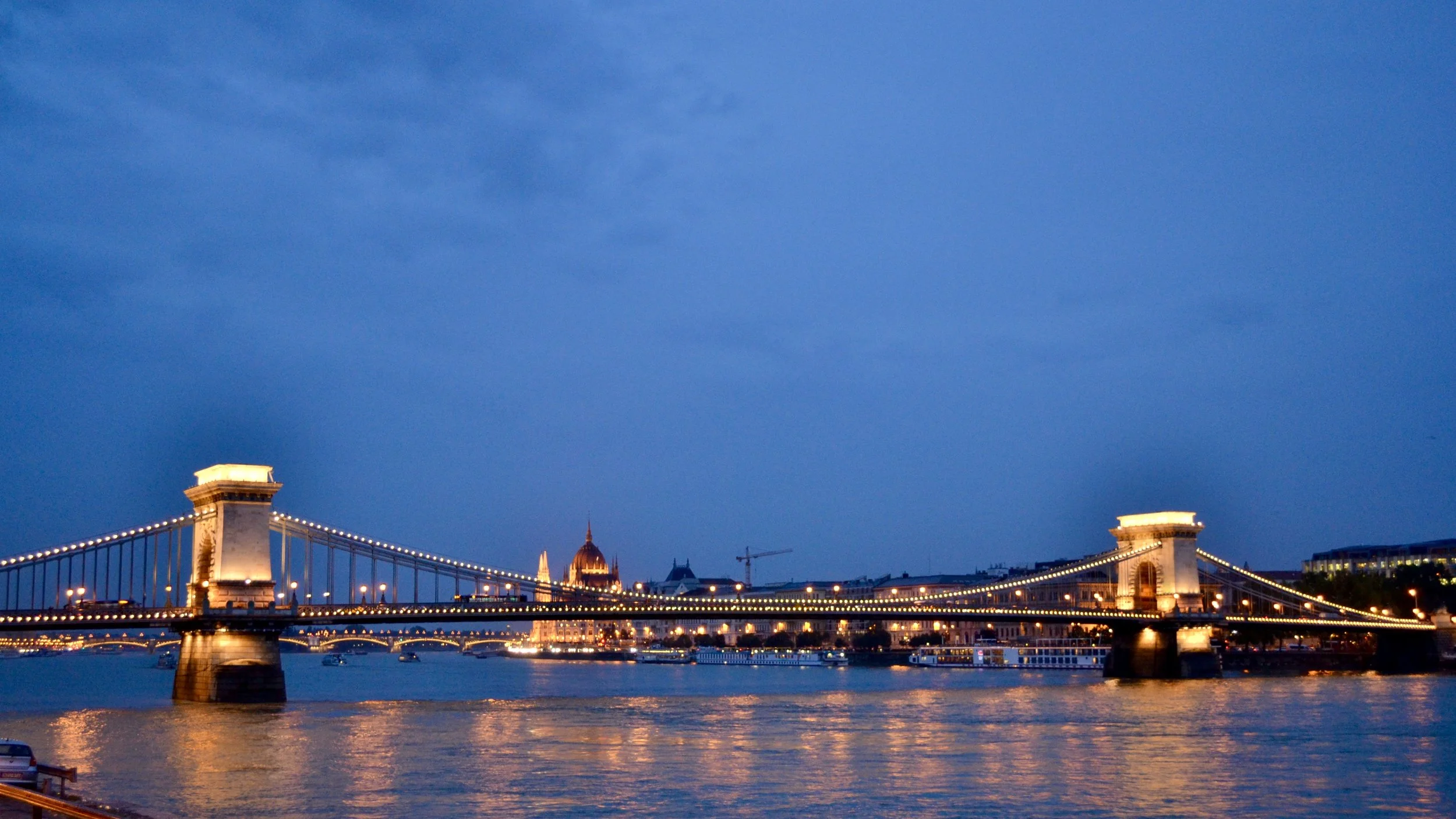 Budapest Széchenyi Chain Bridge at night with Budapest Parliament in the distance.
