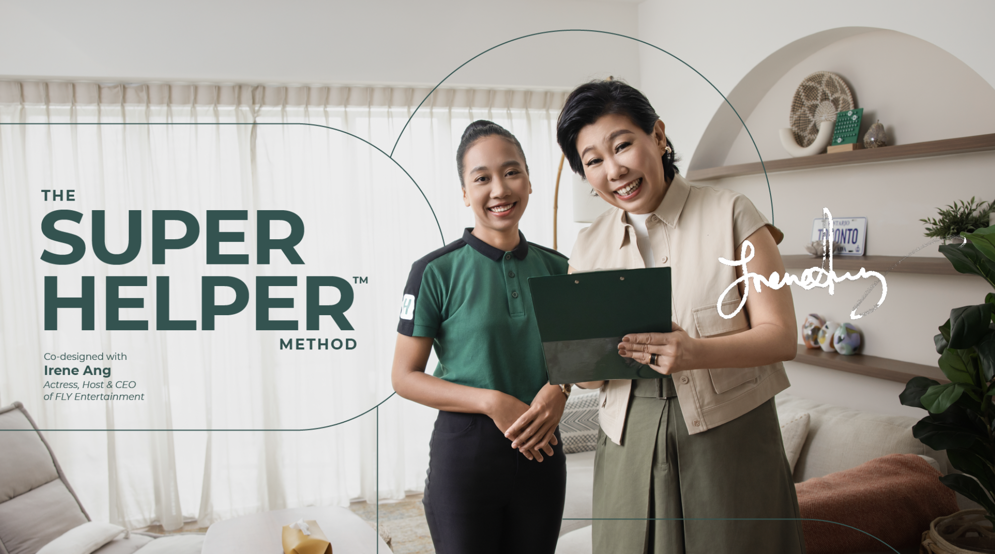 Two women standing in a living room, smiling and looking at a clipboard. One is wearing a green shirt and the other a beige vest. The room has beige walls, a shelf with decorative items, and a sofa with cushions.