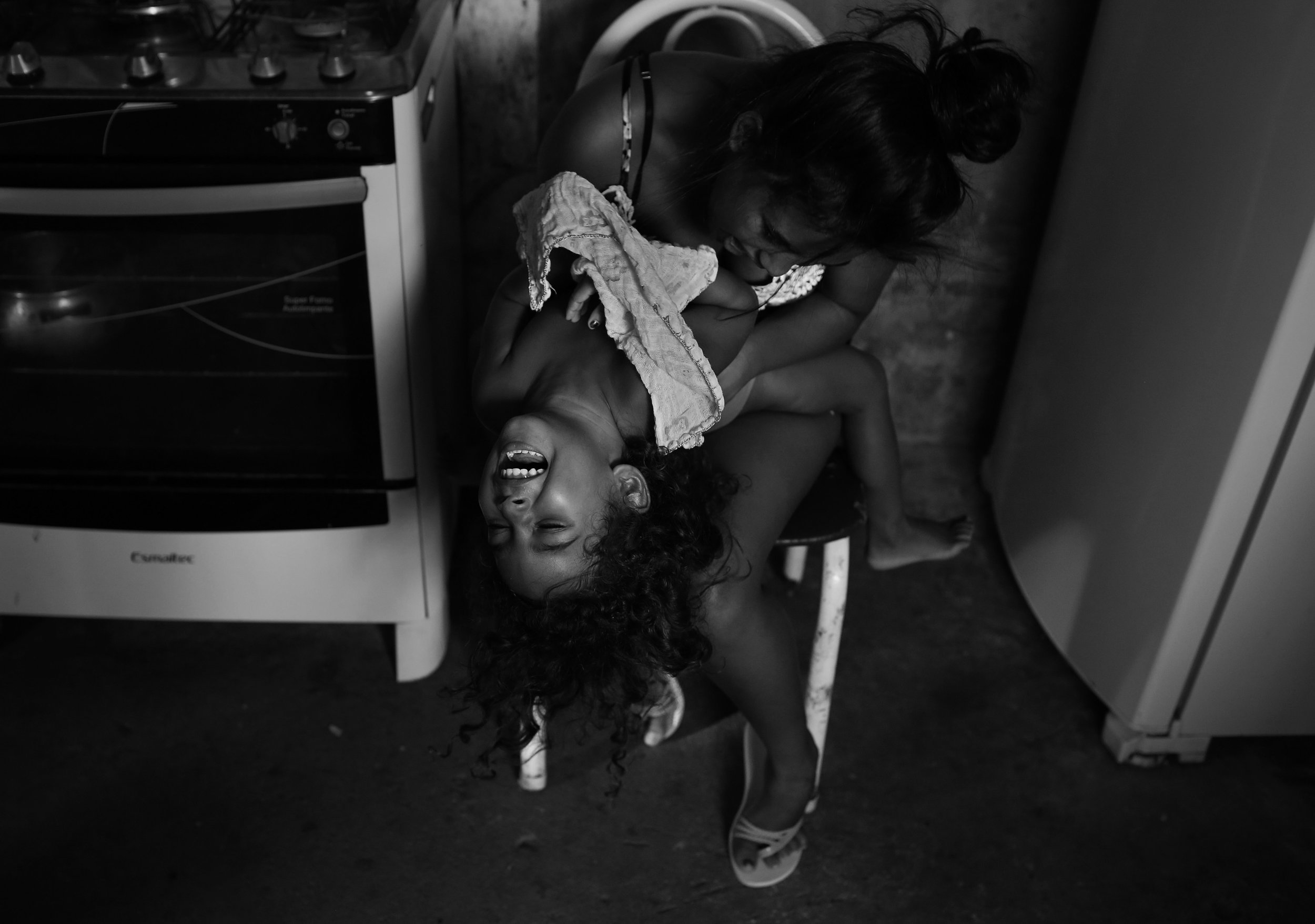  Vivian Amorim, age 4, shrieks with laughter with one of her sisters, Valeria, age 16, in the kitchen of their family’s home. Vivian and Valeria are two of four sisters. Recently a fifth sibling, Samuel, who was born with microcephaly, joined the fam
