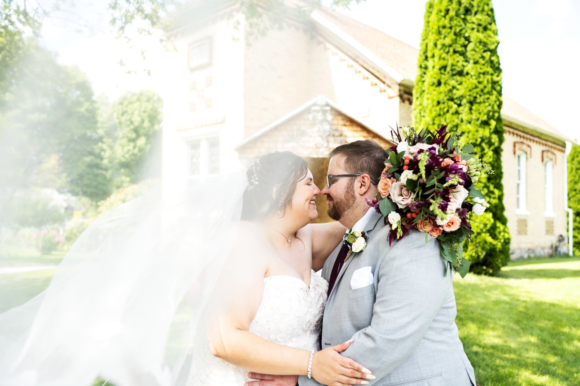 Queer Wedding Couple Nose Rub Kissing Flowing Veil Bouquet in front of Hart Historic Distric Church Session Photo Muskegon West Michigan Grand Rapids MI Box Of Light Photography