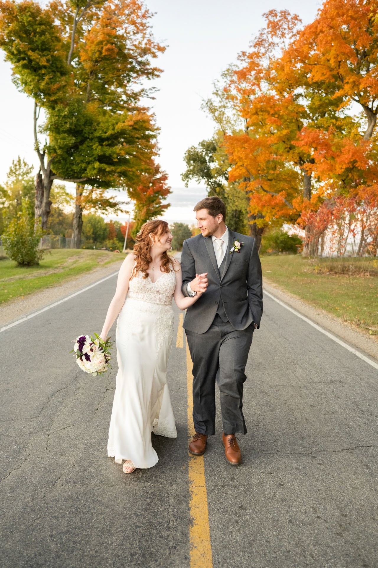 Wedding couple bride groom walking arm in arm down road fall autumn looking at each other Photo Muskegon West Michigan Grand Rapids MI Box Of Light Photography