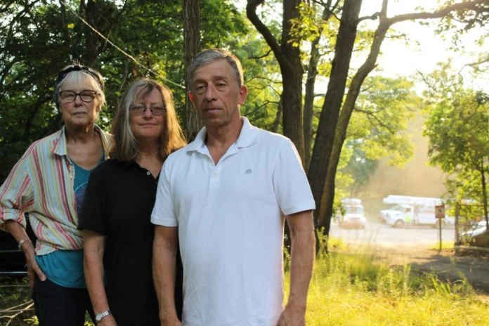 From left, Sandra Ferguson, the vice president of the Friends of the Long Pond Greenbelt, Dai Dayton, the president of the organization, and David Cummings, a board member, all oppose the village's plan to create a police vehicle impound lot on Bridgehampton-Sag Harbor Turnpike, pictured in the background. Christine Sampson photo