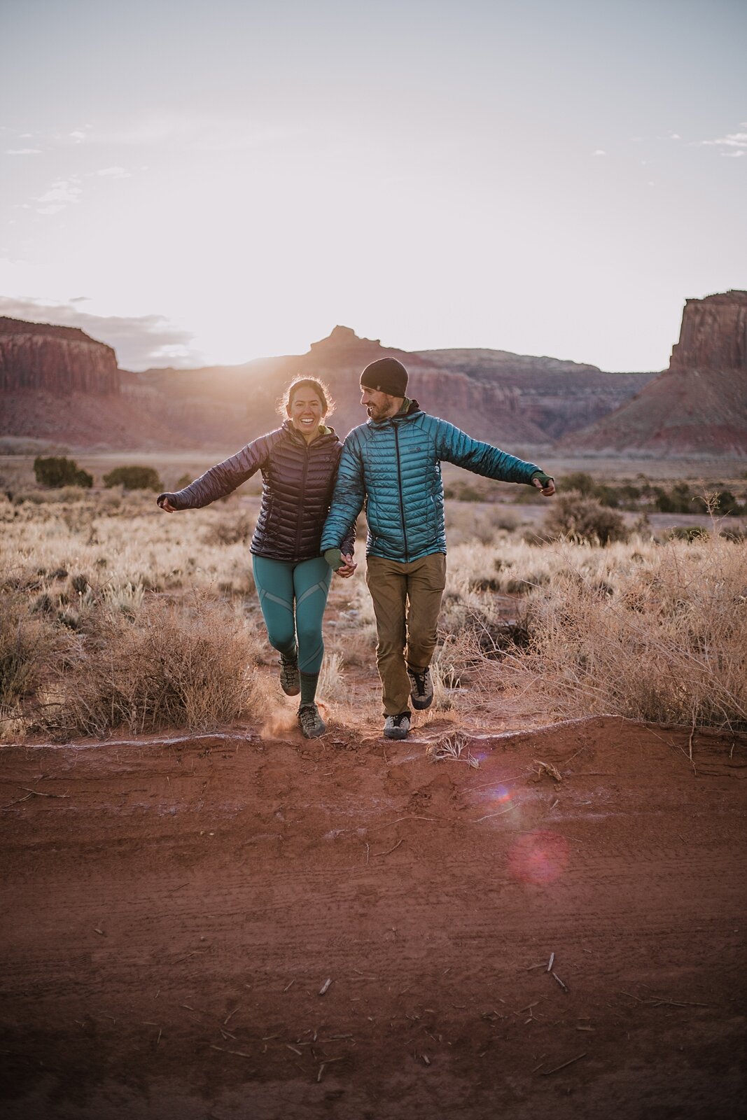 couple hiking through indian creek near monticello utah, indian creek climbing area, canyonlands national park, moab utah engagements, sunrise in moab utah