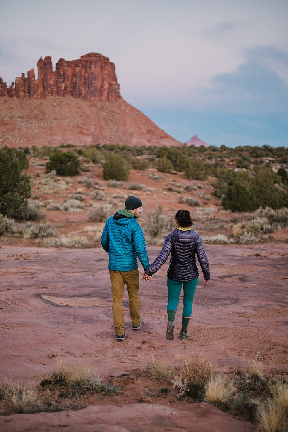 couple hiking holding hands through indian creek, indian creek climbing area, canyonlands national park, moab utah engagements, sunrise in moab utah