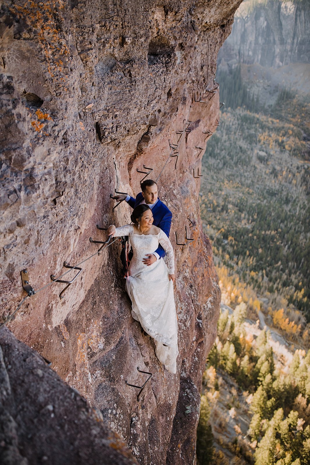 bride and groom hanging on edge of cliff, high alpine elopement, southern colorado hiking elopement, climbing couple, climbing in a wedding dress, hiking in a wedding dress, hiking in a tux