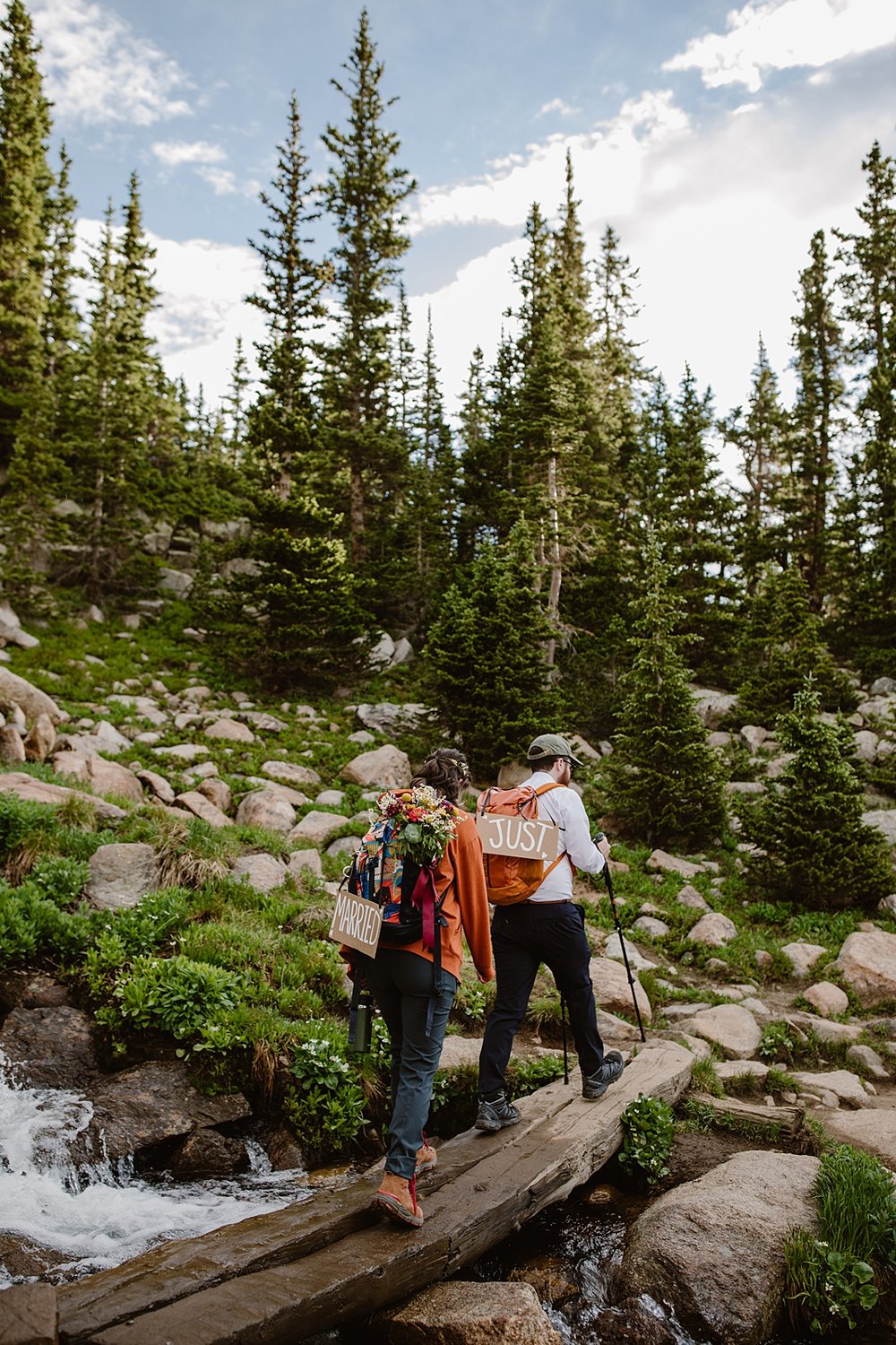 couple hiking down trail, just married handmade elopement signs, pine tree forest, backpacking elopement, high altitude hiking, colorado national forest, wedding bouquet in backpack