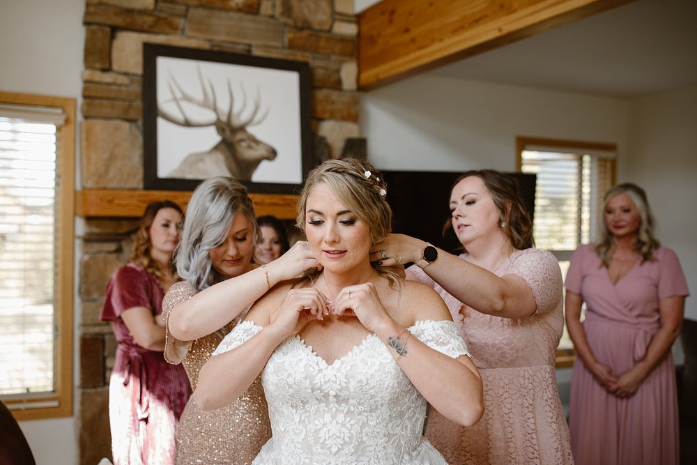 bride putting on necklace, bride celebrating with bridesmaids, breckenridge colorado wedding, breckenridge summer wedding, mountain wedding, summit county wedding, breckenridge airbnb wedding