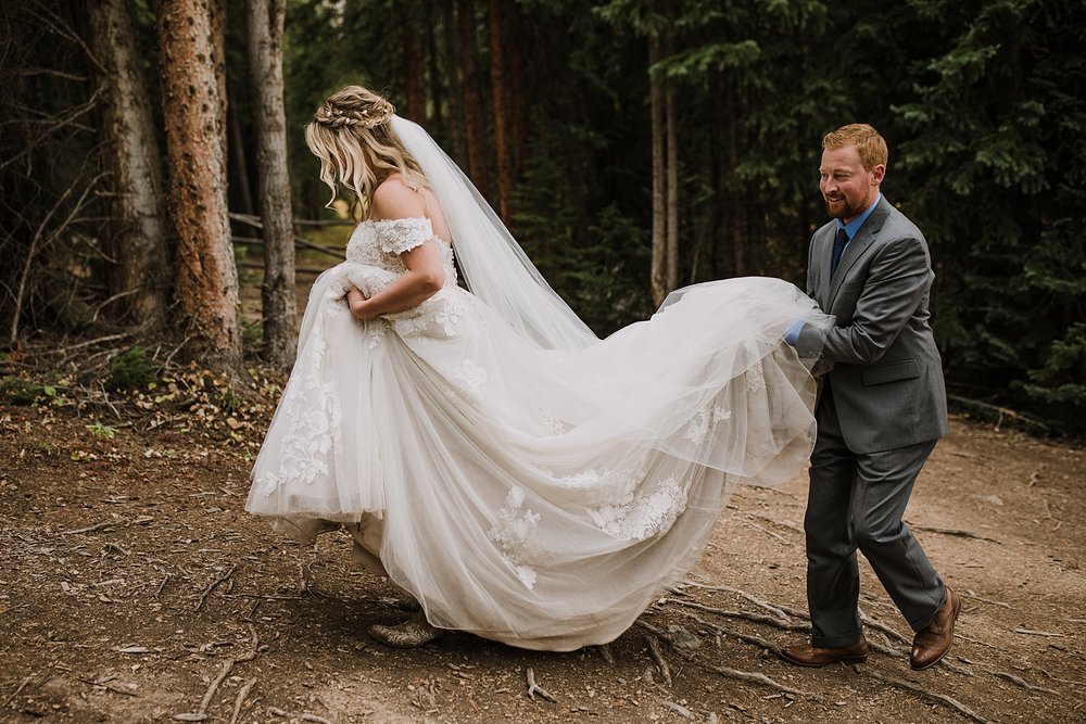 groom helping carry brides gown, bride and groom walking together in a the woods, breckenridge forest wedding, colorado wooded wedding, breckenridge nordic center hiking trails