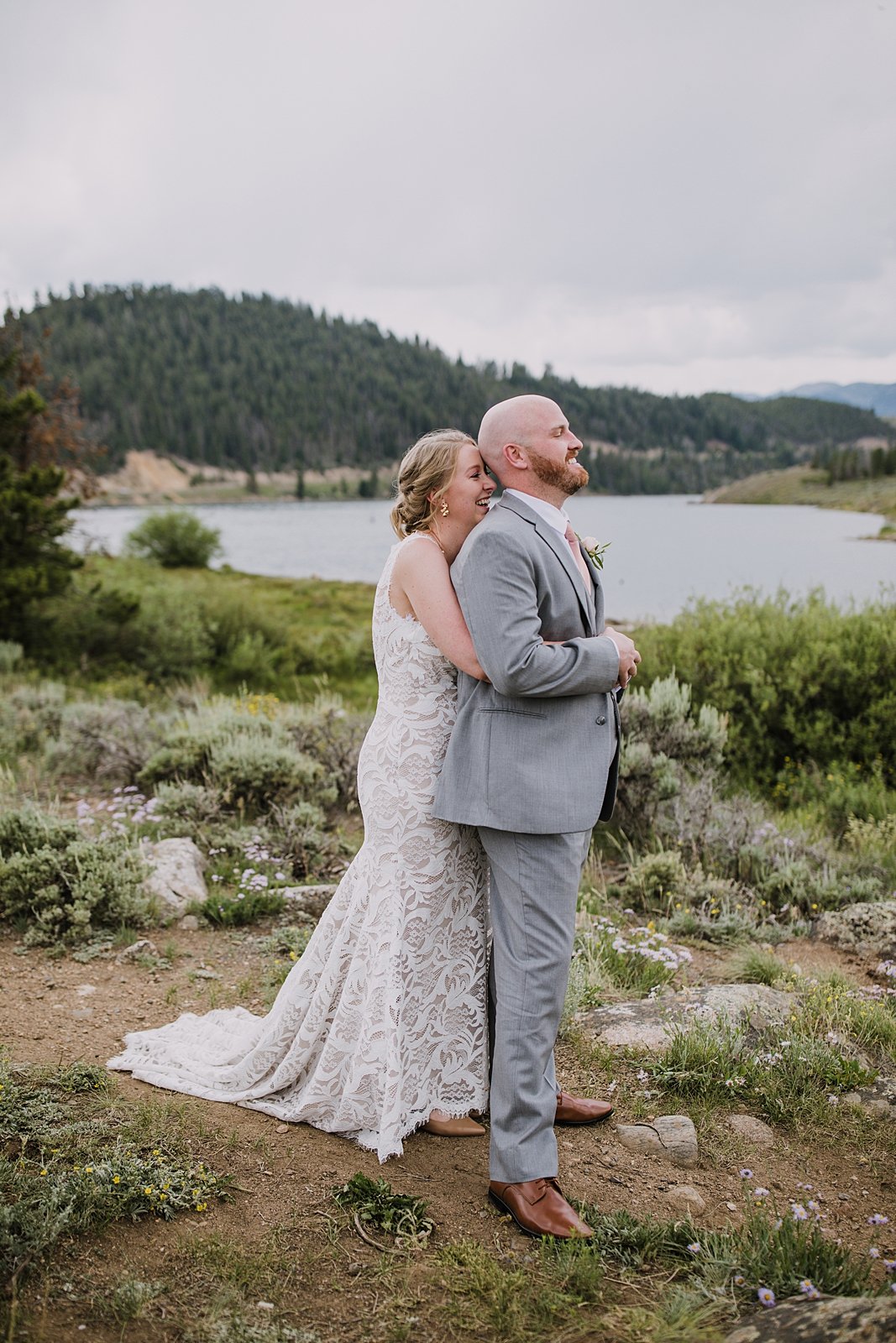 bride and groom standing on lake shore for first look, groom in gray suit, dillon lake reservoir wedding, summit cove wedding, keystone colorado wedding, keystone colorado wedding photographer