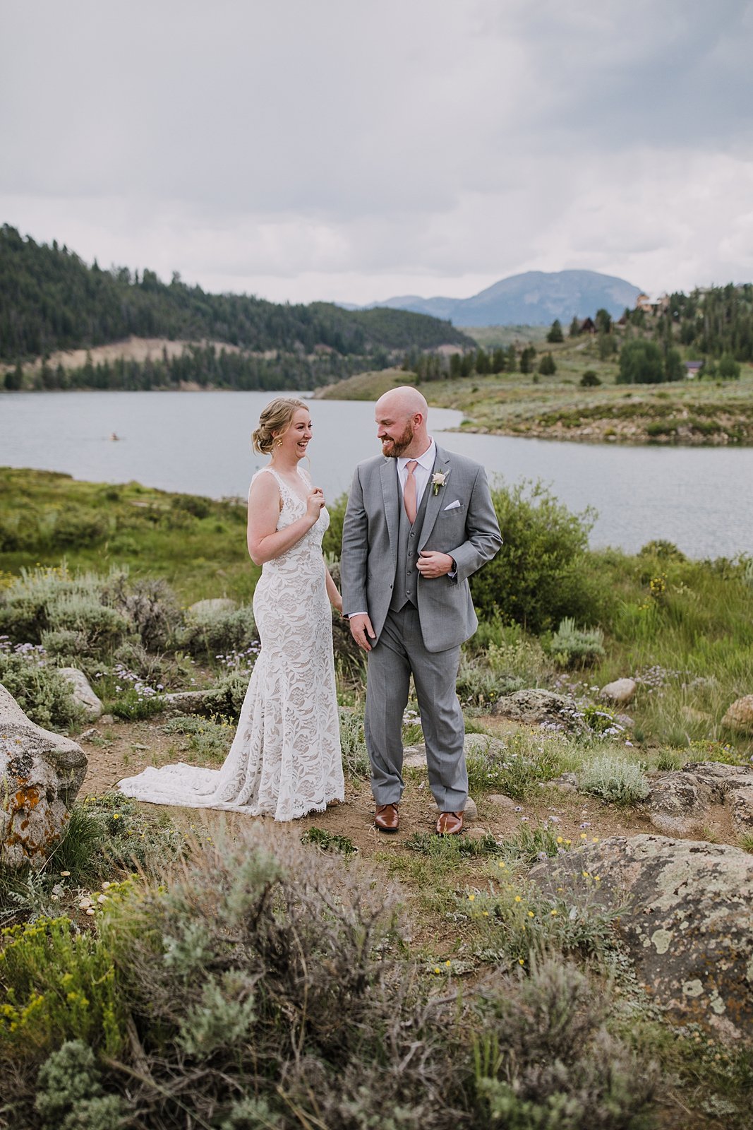 bride and groom standing on lake shore for first look, groom in gray suit, dillon lake reservoir wedding, summit cove wedding, keystone colorado wedding, keystone colorado wedding photographer