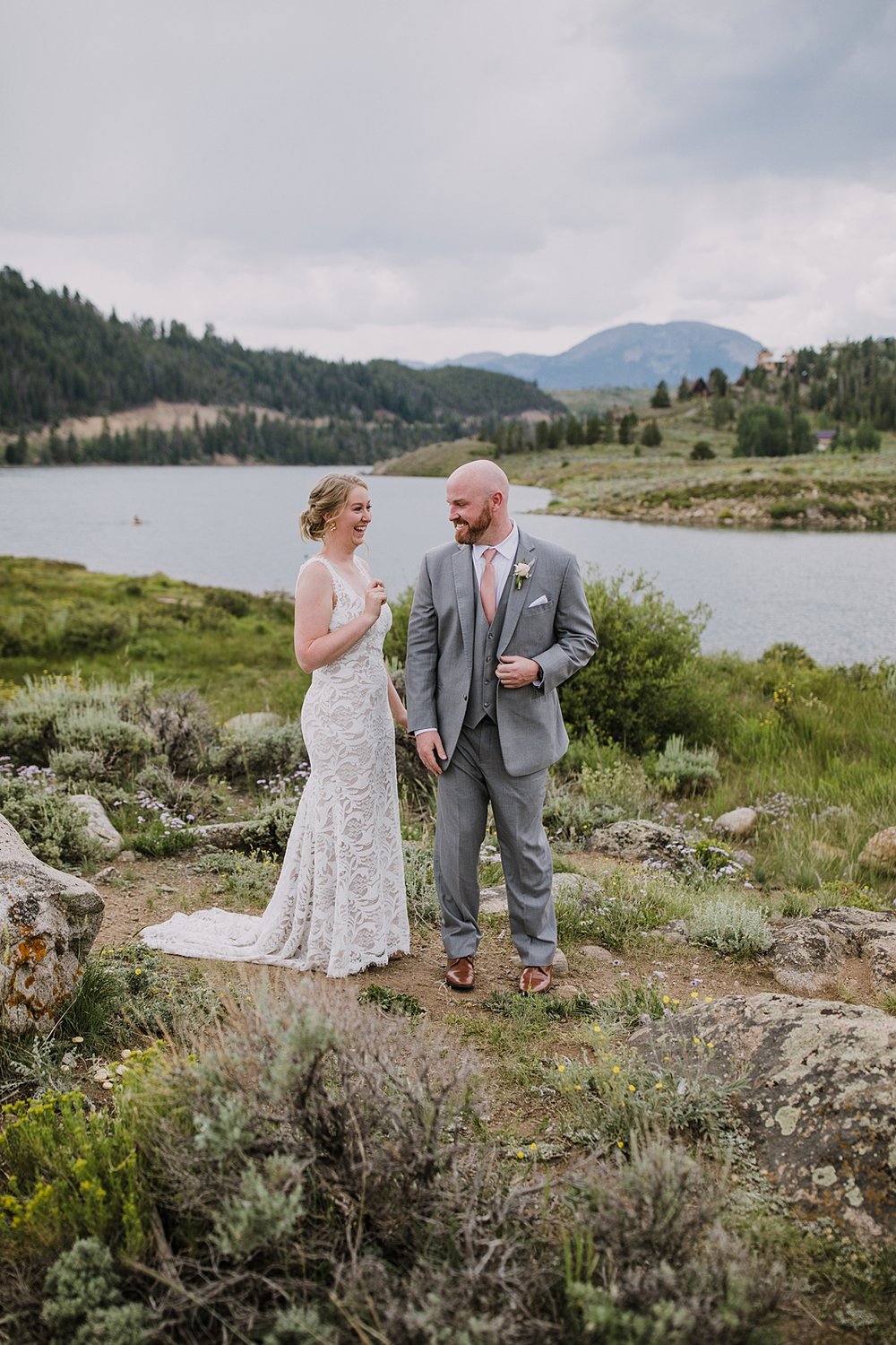 bride and groom standing on lake shore for first look, groom in gray suit, dillon lake reservoir wedding, summit cove wedding, keystone colorado wedding, keystone colorado wedding photographer