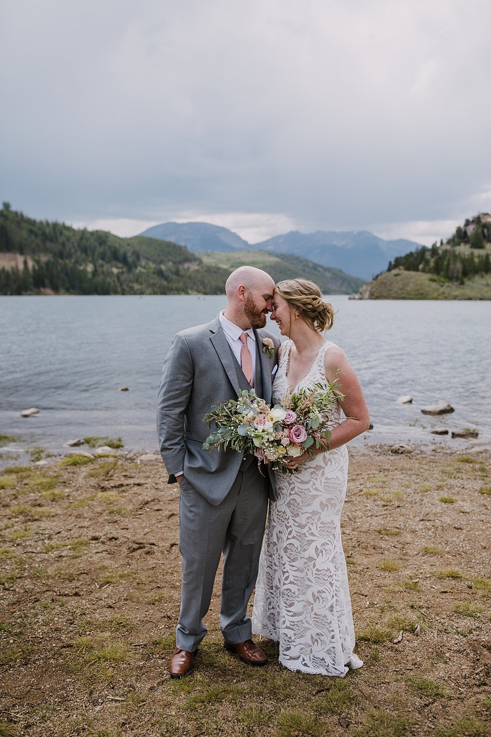 bride and groom walking beside lake dillon reservoir, colorado lakeside wedding, ten mile range wedding, gore range wedding, bhldn wedding dress, gray grooms suit, ten mile range wedding photographer