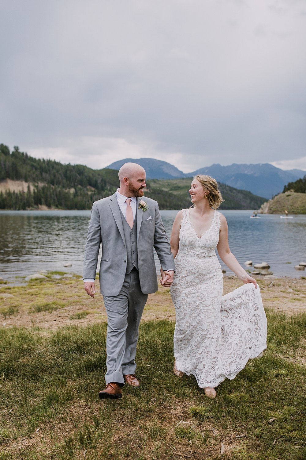 bride and groom walking beside lake dillon reservoir, colorado lakeside wedding, ten mile range wedding, gore range wedding, bhldn wedding dress, gray grooms suit, ten mile range wedding photographer