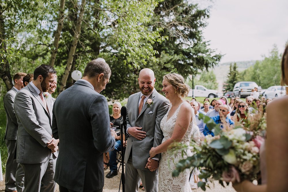 bride and groom laughing with officant, wedding ceremony under trees, silverthorne colorado wedding officiant, silverthorne colorado wedding venue, riverside wedding, river bank wedding, river wedding