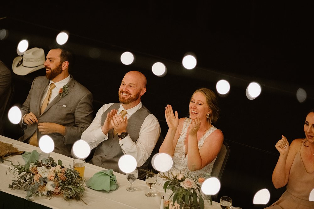 bride and groom clapping during wedding speeches, silverthorne pavilion string lights, silverthorne colorado indoor event space, colorado string light reception space, colorado mountain wedding venue