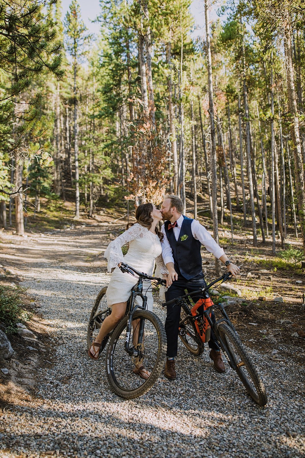 bride and groom riding bikes in wedding attire, mountain biking on your wedding day, couple mountain biking, breckenridge airbnb wedding, breckenridge mountain bike wedding, burnt orange bowtie