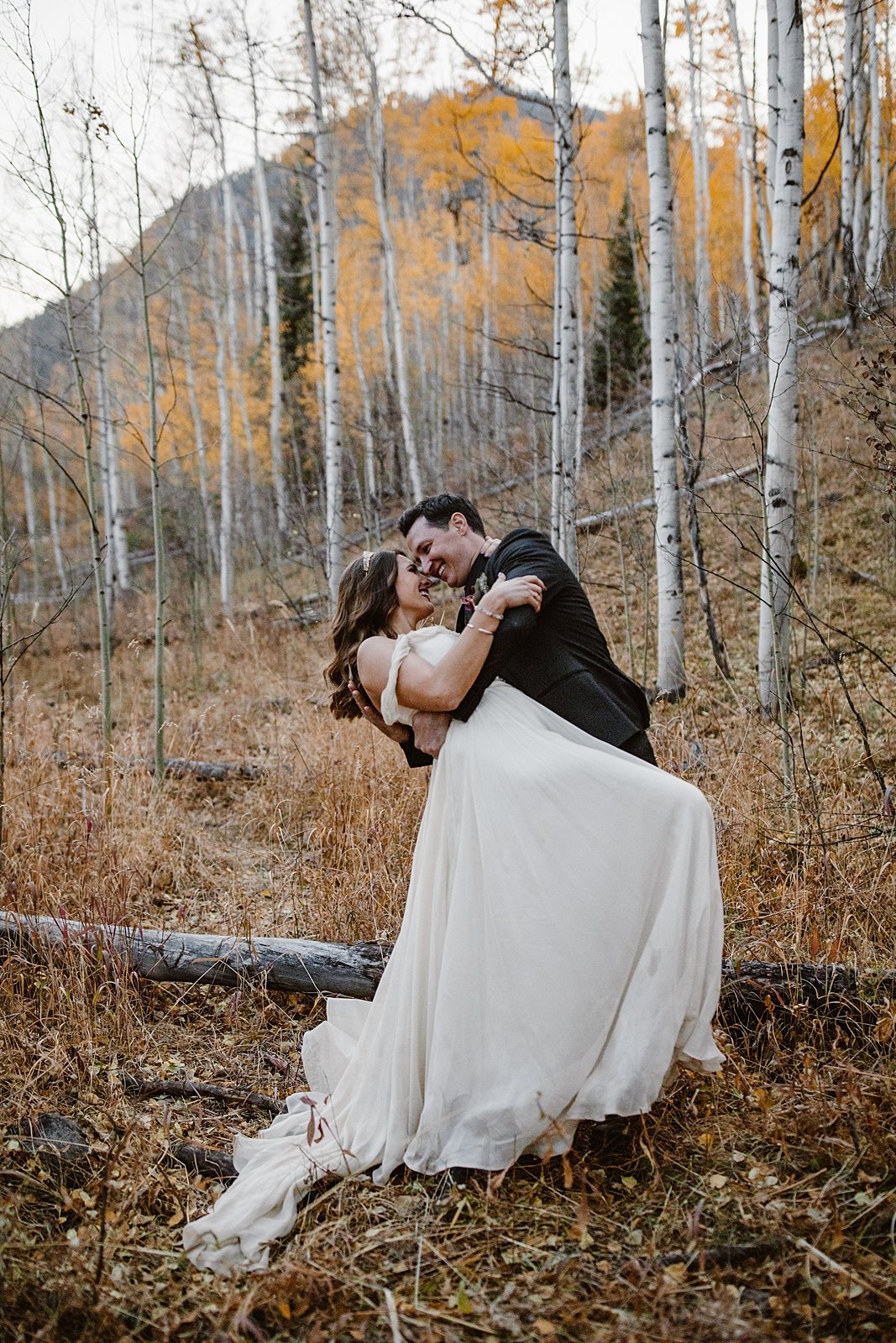 groom dipping bride, breckenridge fall wooded wedding, breckenridge autumn elopement, off the shoulder wedding dress, hiking wedding dress, bridal crystal crown, elope in the changing aspen leaves