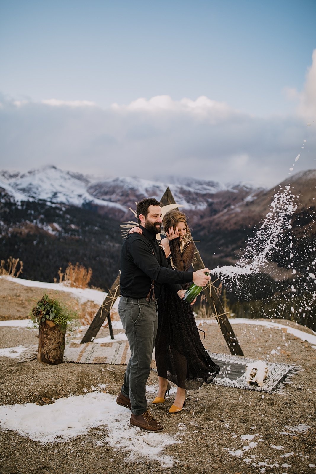 couple popping champagne, mountain top elopement, mountain top ceremony, high alpine mountain pass elopement, high alpine mountain pass wedding ceremony, mountain peak ceremony, dark wedding dress