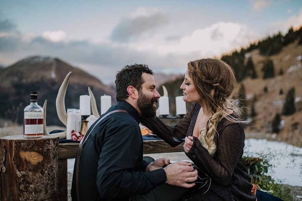 couple laughing while eating wedding cake, black grooms shirt, groom in black attire, twilight mountain elopement, elopement cake, sunset wedding on loveland pass, sunset elopement on loveland pass