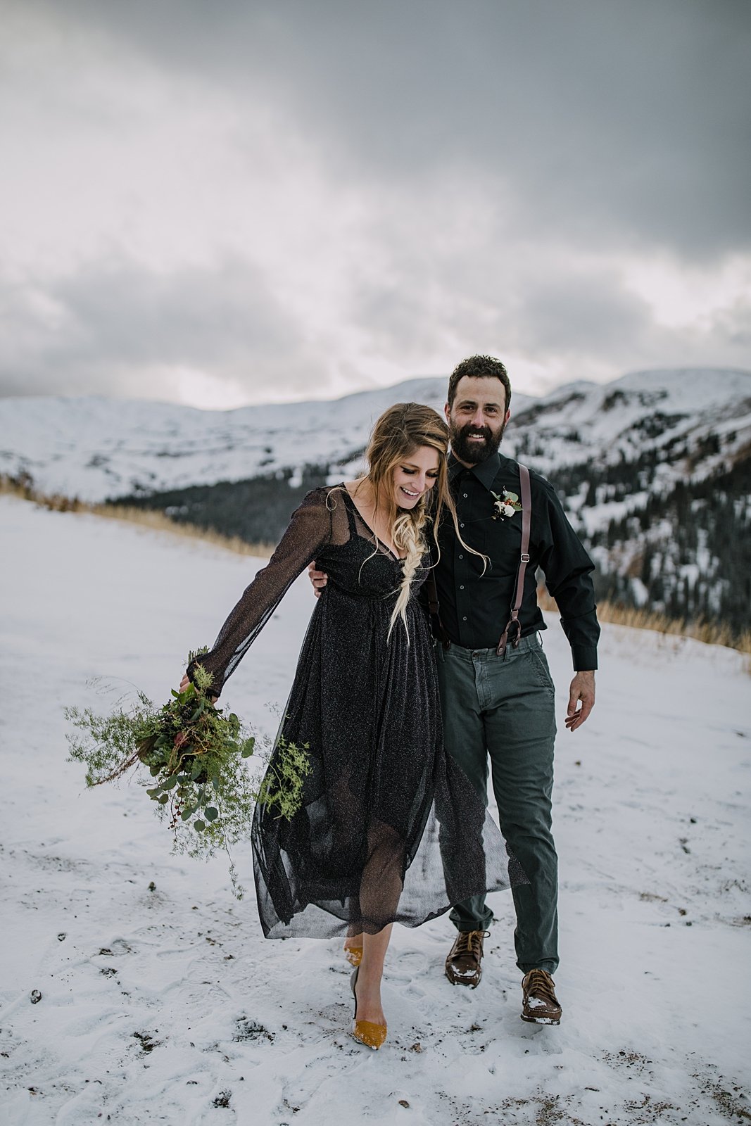 bride and groom walking across snow together, snowy mountainside elopement, whispy fall mountain bridal bouquet, snowy mountain peak wedding backdrop, celestial wedding dress
