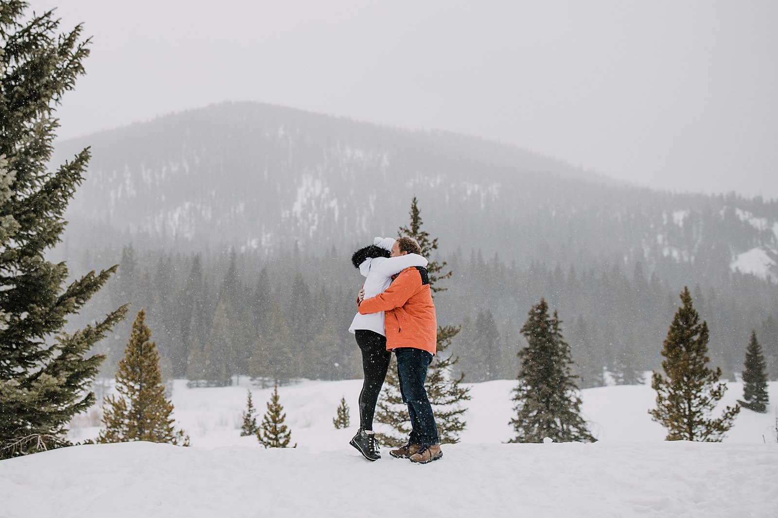 couple hugging in the snow, snowshoe proposal, snowy mountain proposal, breckenridge proposal, swan river valley winter activities, sleigh ride proposal, white winter brides jacket, pine tree proposal