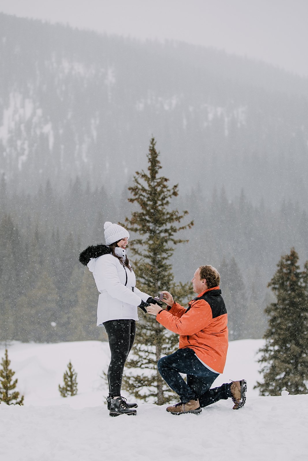 man kneeling to propose in the snow, man proposing in the snow, mountain proposal, colorado mountain proposal, winter proposal, backcountry proposal, bride in black winter boots