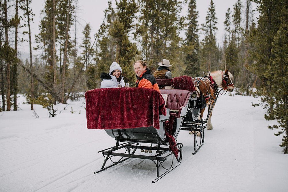 couple toasting champagne on a one horse open sleigh in the woods, open one horse sleigh gliding through the snow, breckenridge spring break proposal, winter bridal jacket, rocky mountain proposal
