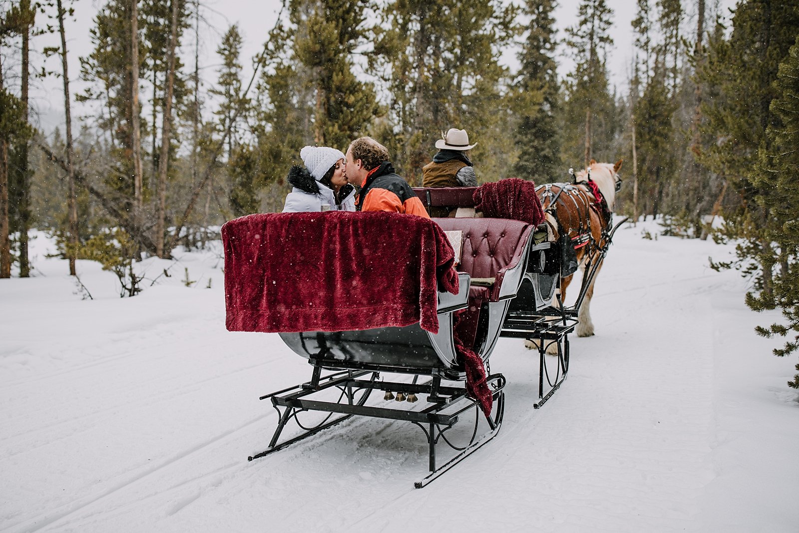couple kissing on a one horse open sleigh in the woods, open one horse sleigh gliding through the snow, snowy breckenridge spring break proposal, winter bridal jacket, rocky mountain sleigh ride