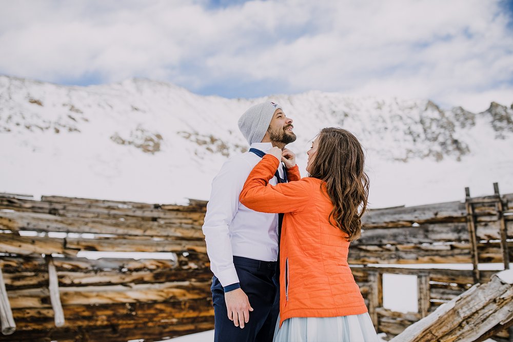 bride fixing grooms shirt and tie, getting dressed in a miners cabin, navy blue winter wedding, wedding in the mountains, elopement in the mountains, colorado cabin relic, navy blue elopement colors